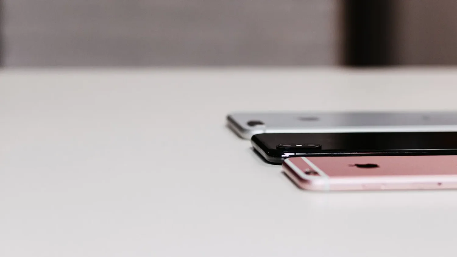 Розовый и серебристый iPhone на белом столе