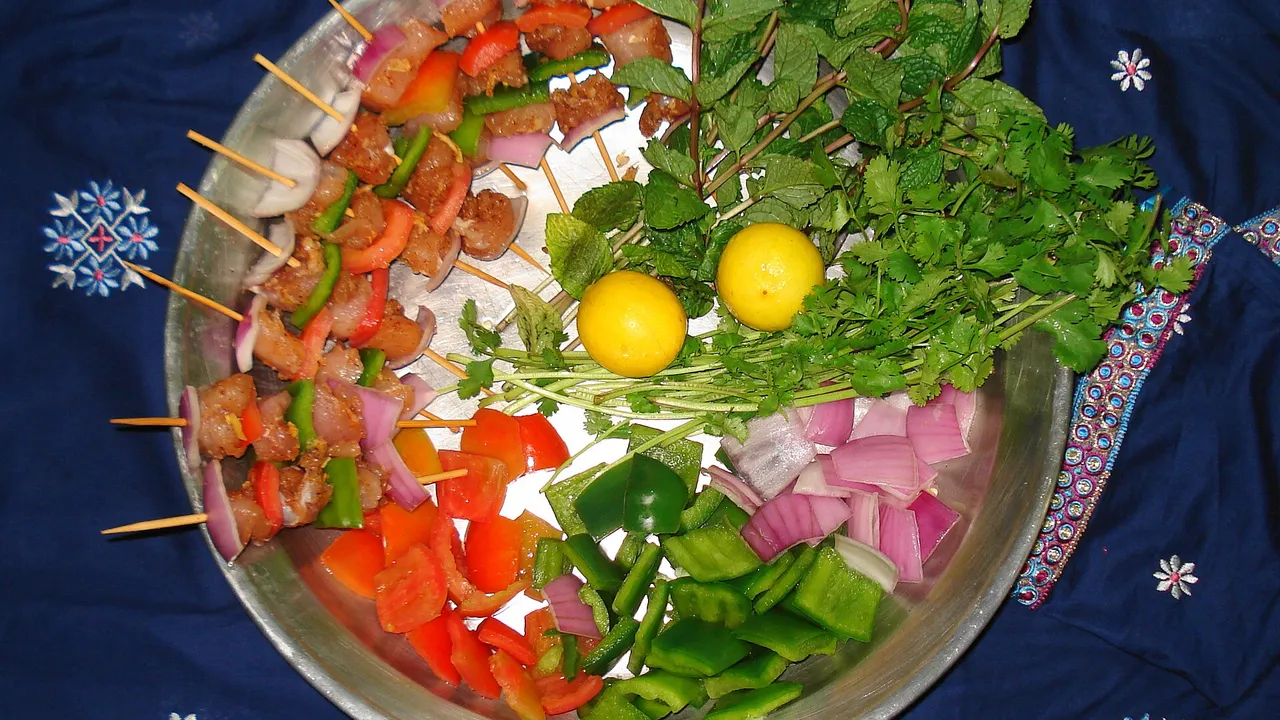 Ингредиенты для шашлыка: сырое мясо на шпажках, перец, лук, зелень и лимоны на подносе