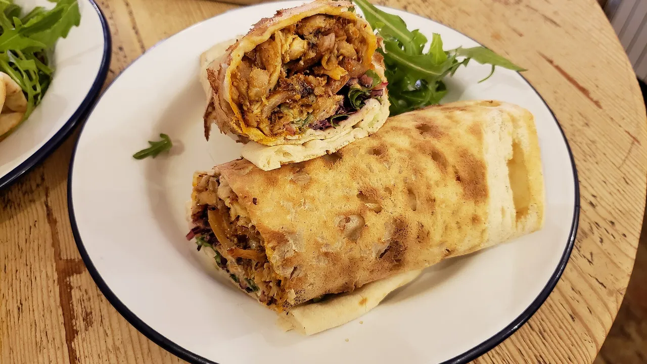 Две половинки шаурмы в лаваше с курицей и овощами на белой тарелке, рядом листья рукколы