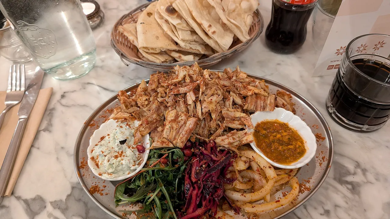 Блюдо с нарезанной курицей шаурмой, маринованной капустой, луком, соусами и картофелем фри, рядом стопка лепёшек
