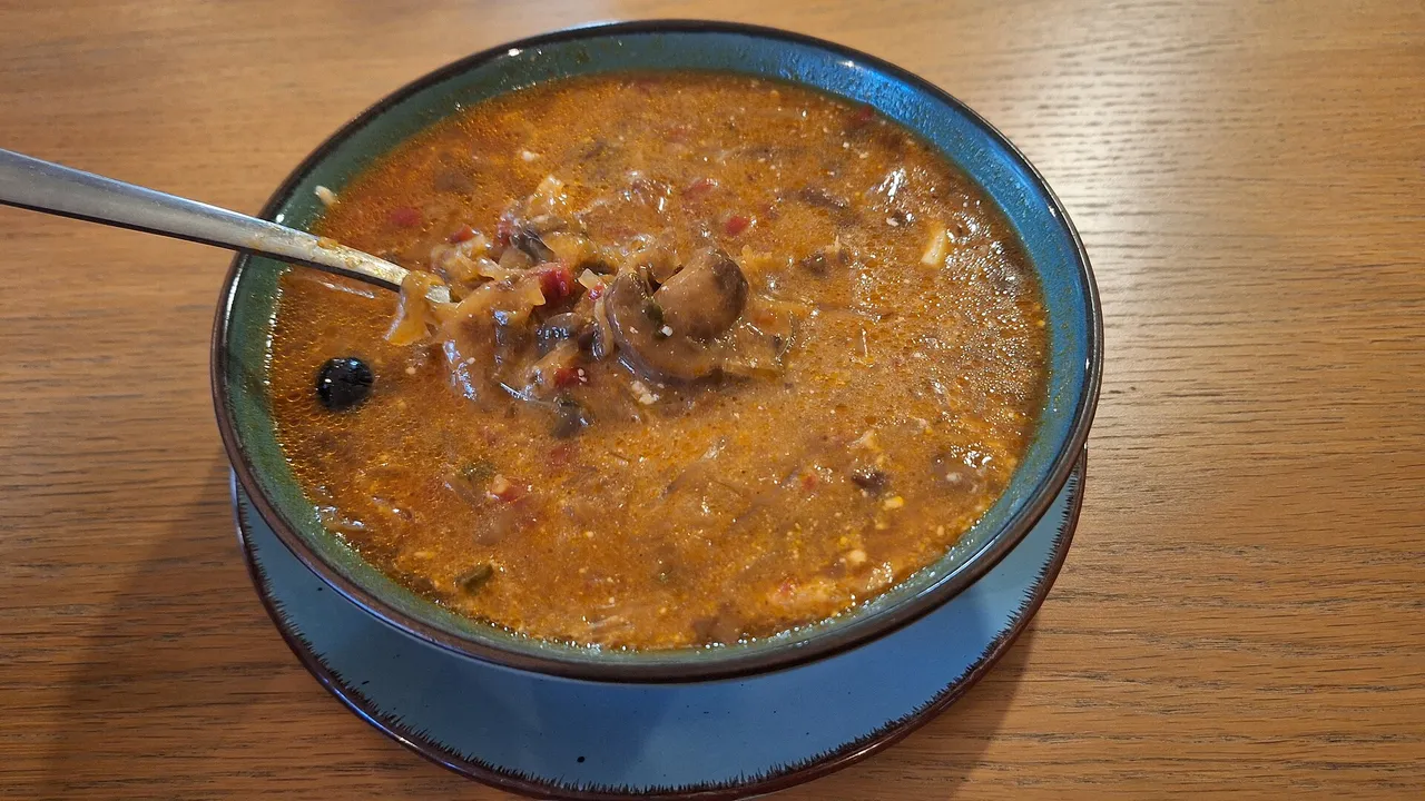 Густая солянка с грибами и маслиной в голубой глиняной миске с ложкой на деревянном столе